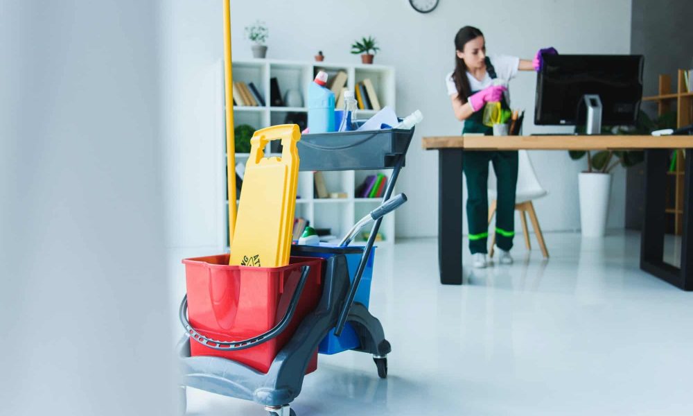 young-female-janitor-cleaning-office-with-various-cleaning-equipment.jpg